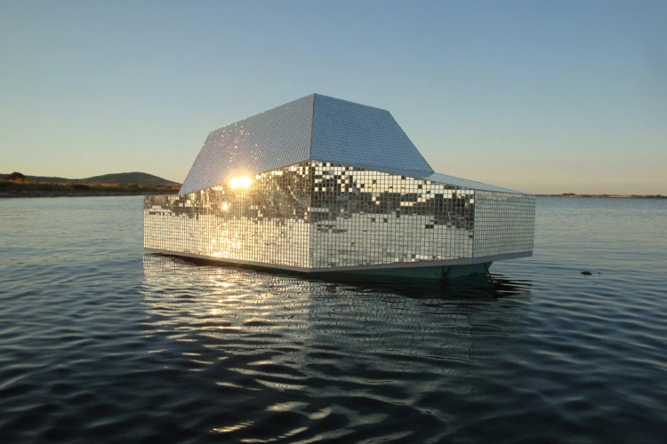 Duck dance - « Duck Dance » est une sculpture hybride d'affut de chasse flottant et de boule à facette. Cet abri flottant est un archétype de micro-architecture vernaculaire, la plupart du temps auto-construit et bricolé avec inventivité, conçu avec soin pour s'intégrer dans son environnement naturel / sa nature sauvage (camouflage adapté, géométrie / volumétrie furtives évoquant les avions militaires F-117, etc) et répondre aux besoins physiques et ergonomiques minimums du prédateur de col vert (protection contre les éléments et la vue, positions possibles assis, accroupi ou allongé…) Pour le visiteur consommateur de paysage, c'est finalement plus une composante esthétique récurrente de l'image bucolique du territoire, qu'une typologie fonctionnelle et utilitaire du chasseur occitan, usager régulier du canardage de gibier d'eau, régulièrement pratiqué dans les étangs, lagunes et marais languedociens (notamment l'etang de Thau, débouché Est du Canal du Midi). Et c'est aussi une invitation à parcourir le canal en suivant ce riche corridor écologique, notamment utilisé par les canards… Ici, la texture « boule à facette », comme icône, nous renvoie à la fête, la boîte de nuit, la chaleur de la danse, tout en offrant une autre façon de se cacher dans un contexte, en donnant un reflet, multiple et fragmenté de l'environnement, un camouflage sémantique adaptatif… Pour disparaître, je brille, je me sur-expose, je rayonne… - Microclimax - Carolyn Wittendal - Benjamin Jacquemet 